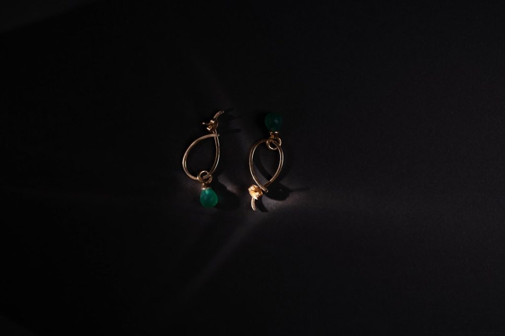 Gold earrings with green beads on black background