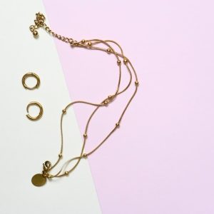 Gold necklace and earrings on pastel background.