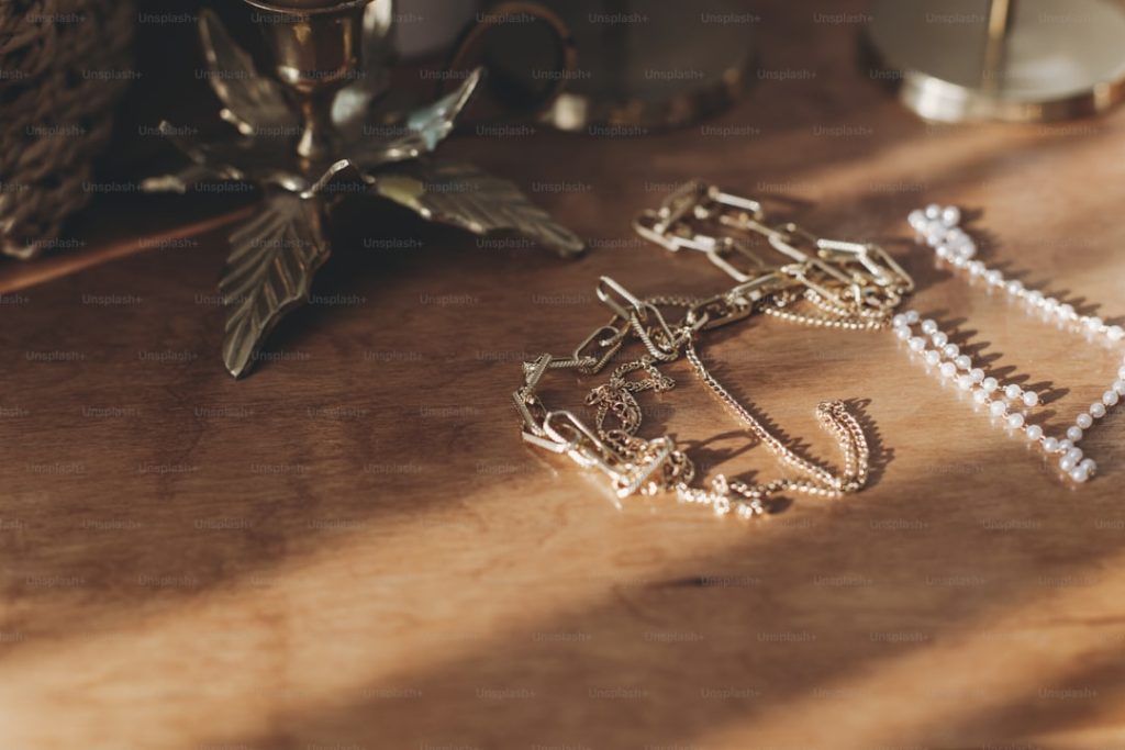 Modern gold and pearl accessories on table with vintage candlesticks. Stylish golden necklace and ring on wooden background in sunny light.