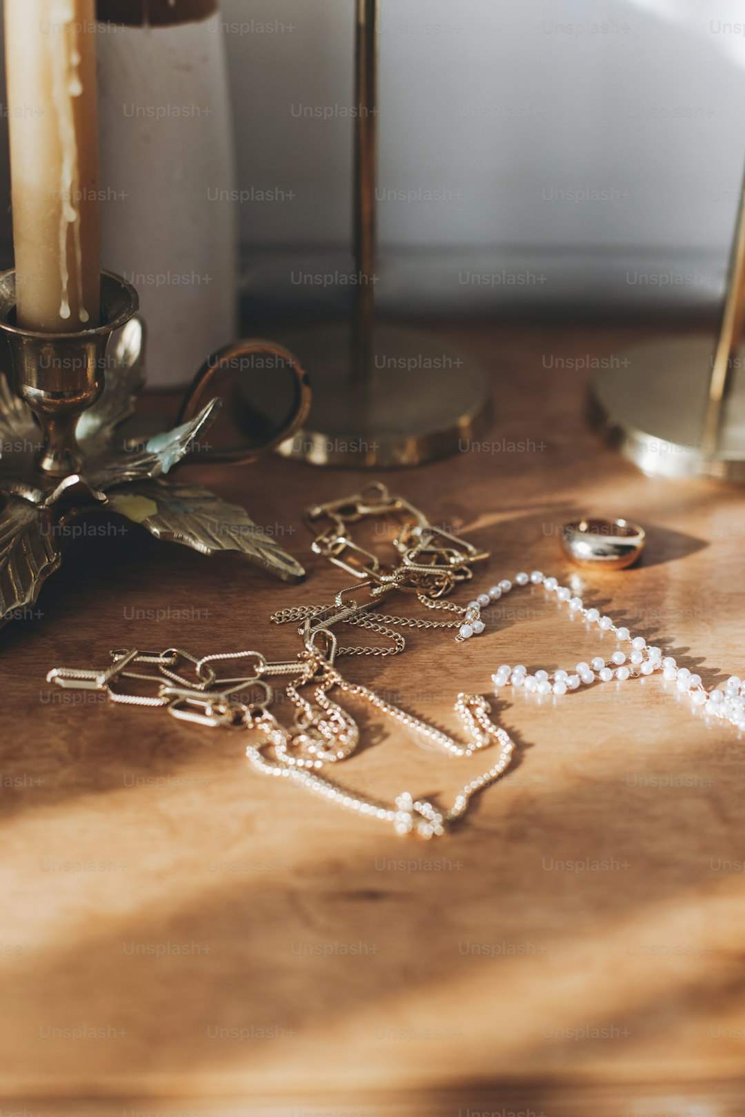 Modern gold and pearl accessories on table with vintage candlesticks. Stylish golden necklace and ring on wooden background in sunny light.