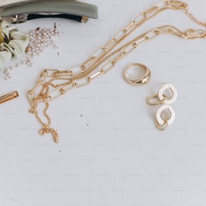 Modern golden jewellery, hair clips, barrettes on white table. Stylish gold ring, chain necklace, earrings, hairbands. Summer Boho accessories