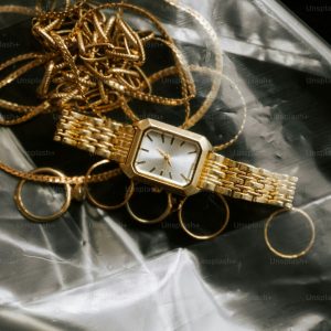Gold watch and jewelry on plastic wrap.